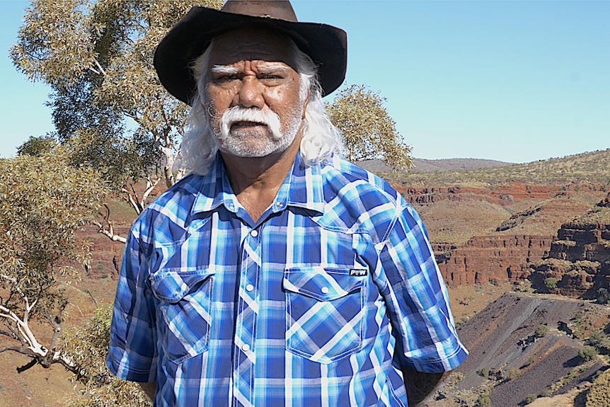 An elderly man standing in front of a tree