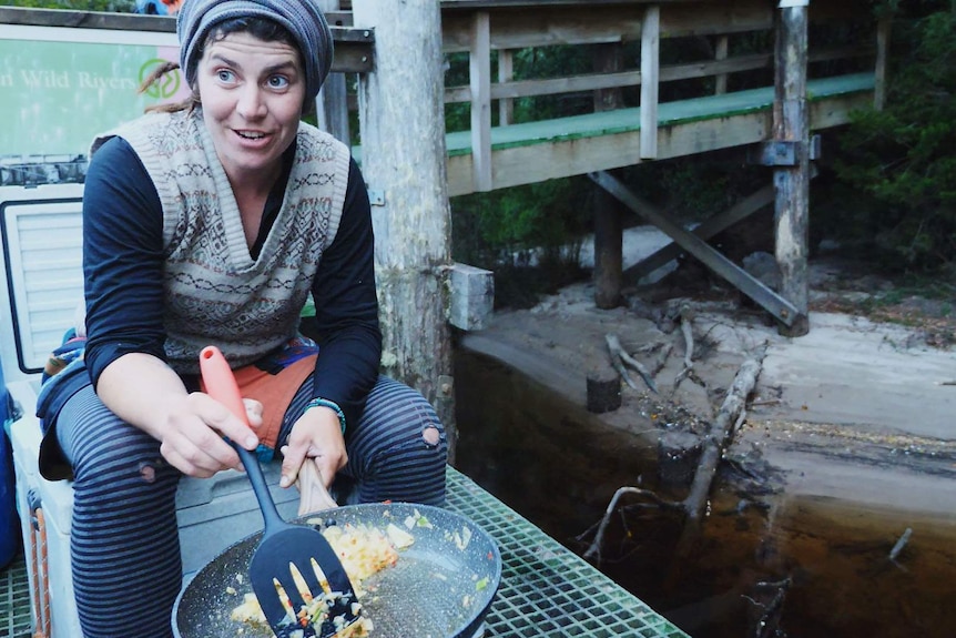 River guide seated on a jetty, cooking stir-fry on a little gas cooker