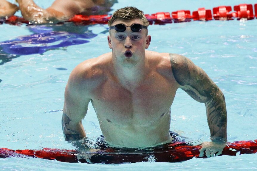 Adam Peaty leaves his mouth agape as he pulls his torso above the water line as he leans on pool lane markers.