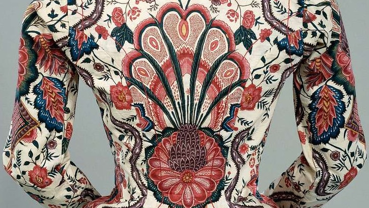 You view the rear of a mannequin which wears a boldly patterned chintz jacket billowing over an A-line skirt.