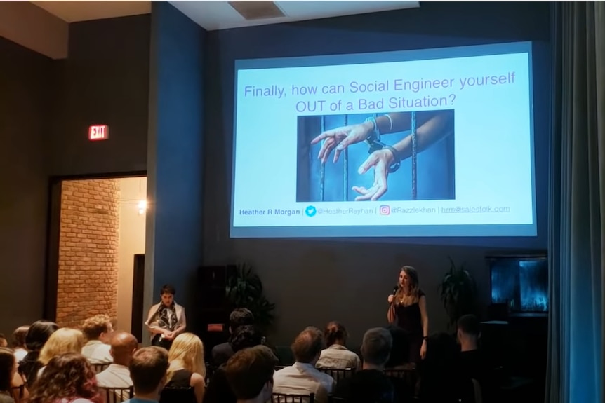 A woman speaks into a microphone in front of a screen with "Finally, how to social engineer your way OUT of a bad situation"