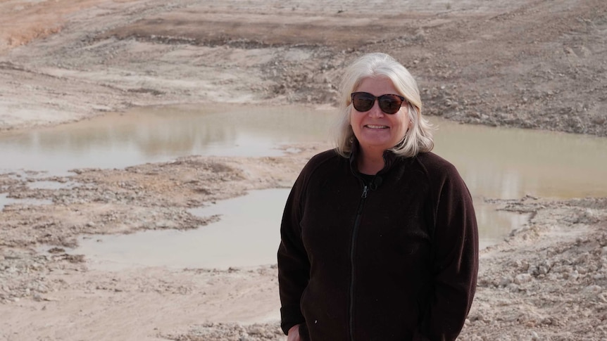 A woman stands in front of an empty dam.