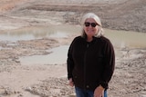 A woman in sunglasses stands in front of an empty dam