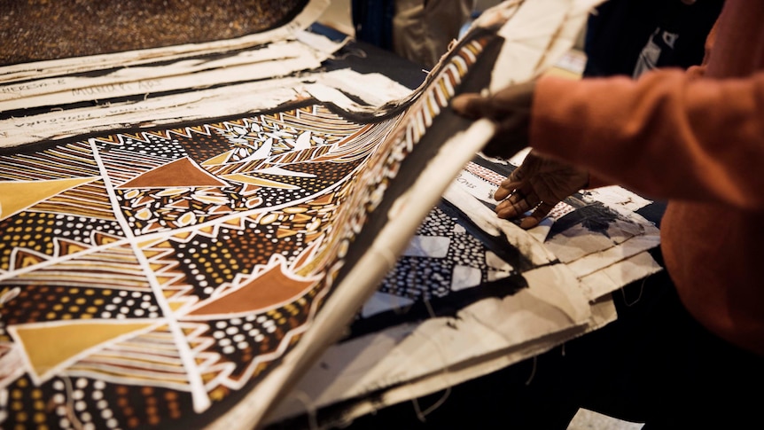 A stack of indigenous art paintings being sorted through by two hands
