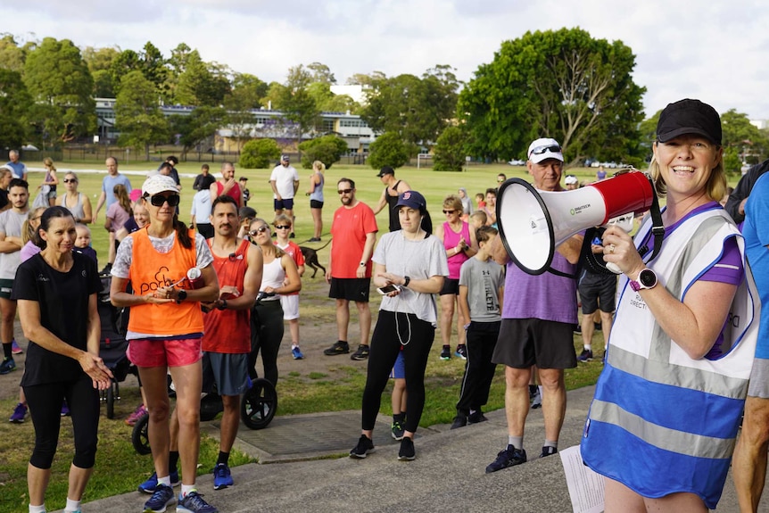 A woman with a megaphone looks at the camera and smiles while a group of people stand and listen.