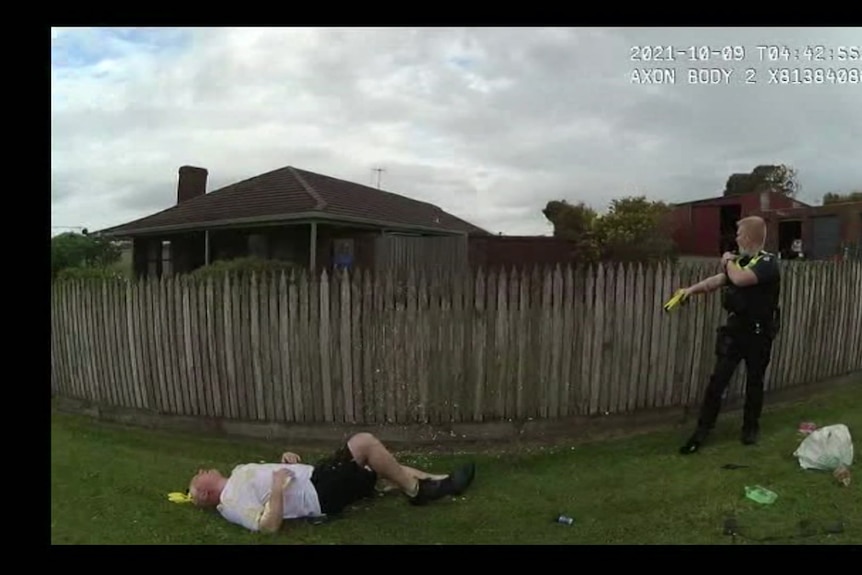 A man lies on the ground after assault as police officer points at him