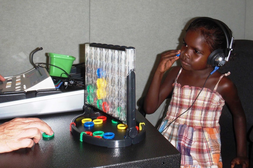 An Indigenous child with headphones on listening to instructions and thinking about where to put a coloured token.