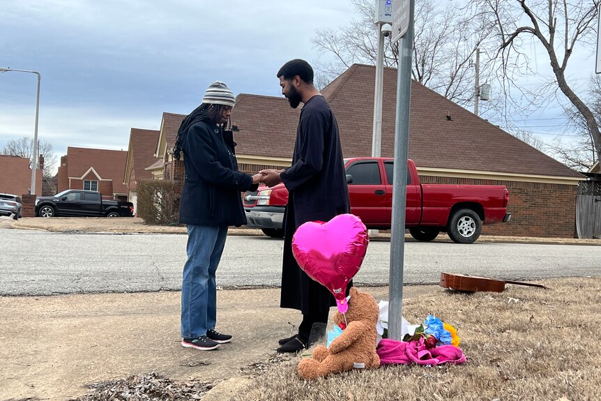 A man and woman pray at the site where Tyre Nichols was beaten, where there are toys on the ground