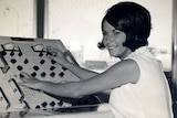 A black and white picture of Lauri Glocke smiling while working at a control panel.