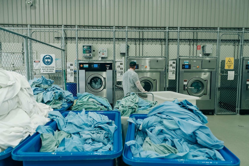 A prisoner uses a laundry with blue sheets in baskets in front.