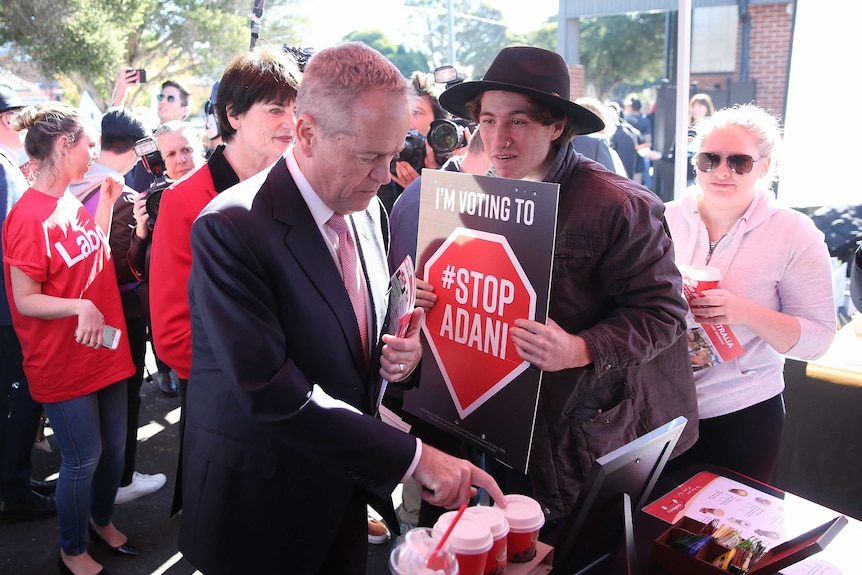 Shorten is pointing at a coffee size as the protester holds a Stop Adani sign centimetres from him.