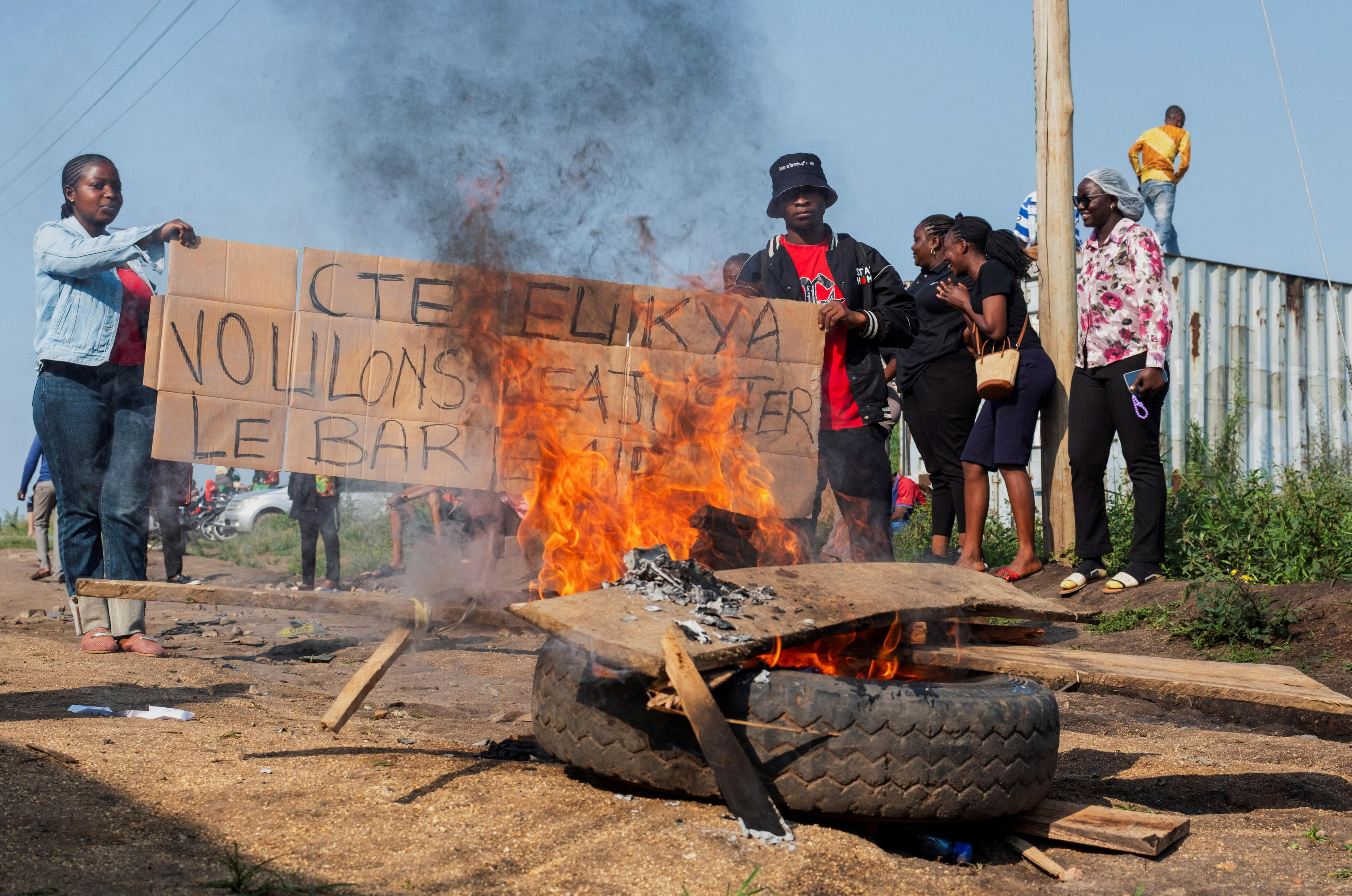 Young men and women holding a sign in front of a burning tyre on the street.
