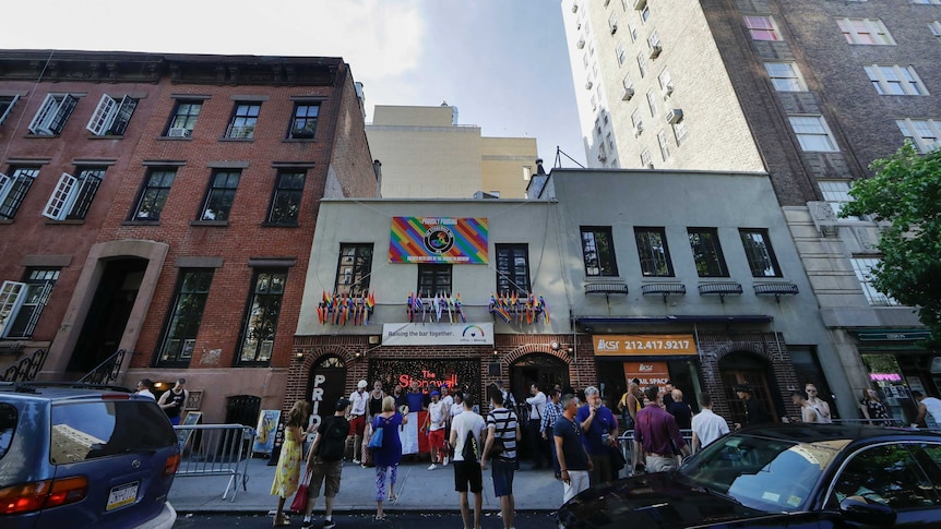 People take photos outside the Stonewall Inn which has multiple rainbow flags hanging out its windows