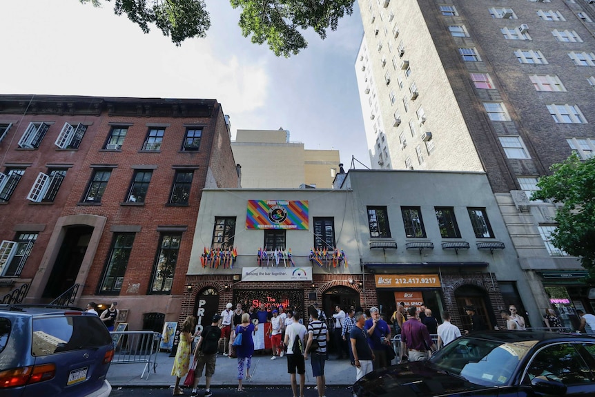 People take photos outside the Stonewall Inn which has multiple rainbow flags hanging out its windows