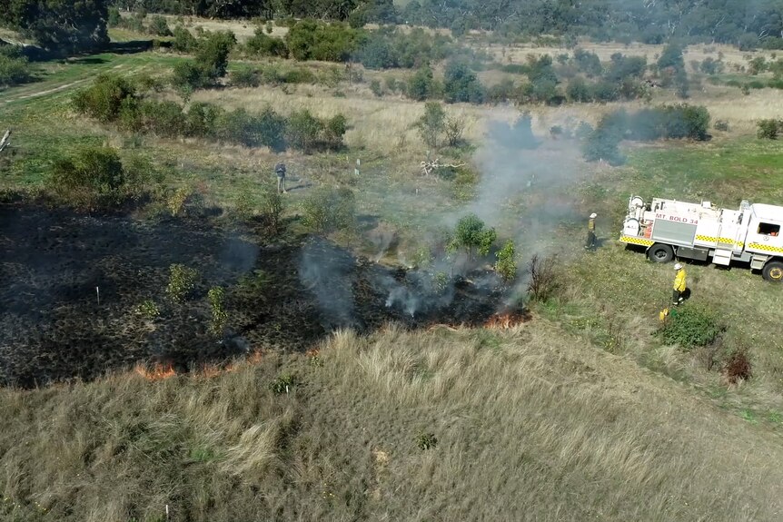 A grass patch burn with a truck and firefighter in the top right-hand side of the frame