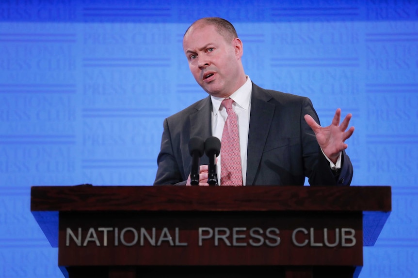 Frydenberg is standing at a podium that says National Press Club. He is talking, left arm raised.