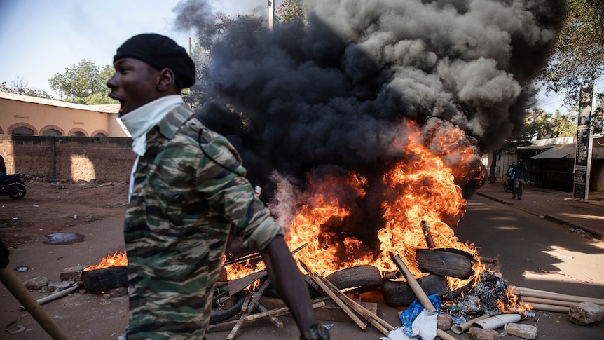 A man yells as he walks past a pile of burning tyres.
