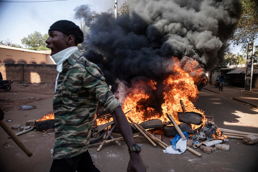 A man yells as he walks past a pile of burning tyres.