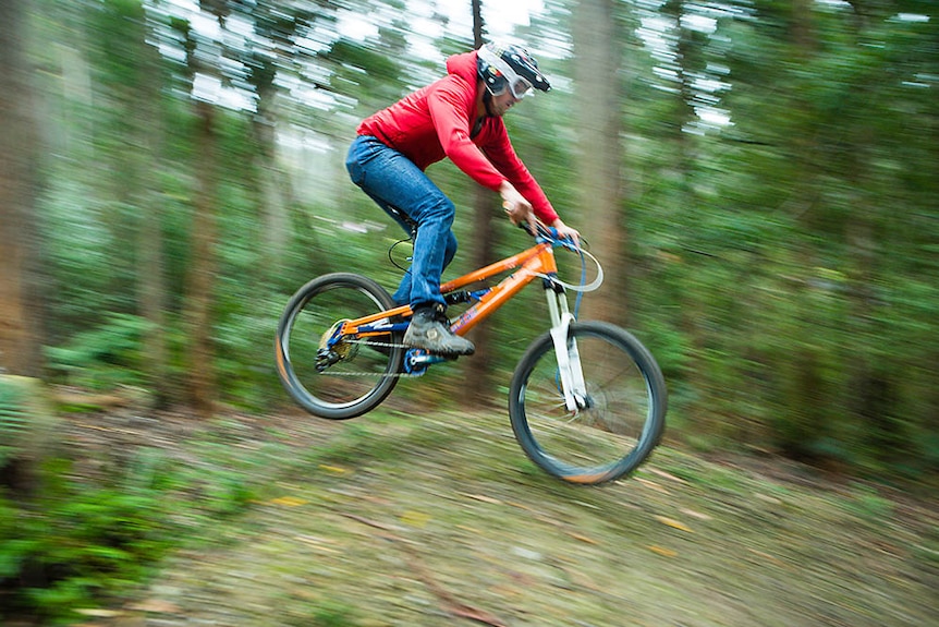 man jumping a mountain bike in very green forest
