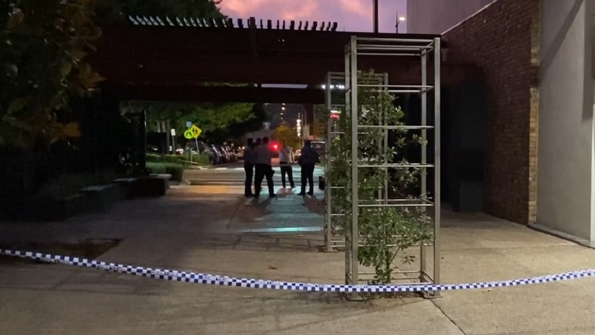 Police tape marking a crime scene with police officers in the background