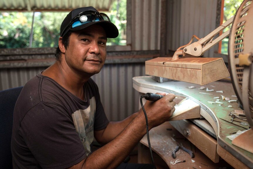 A mid shot of West Kimberley artist Garry Sibosado at an art bench posing for a photo carving a design into a pearl shell.