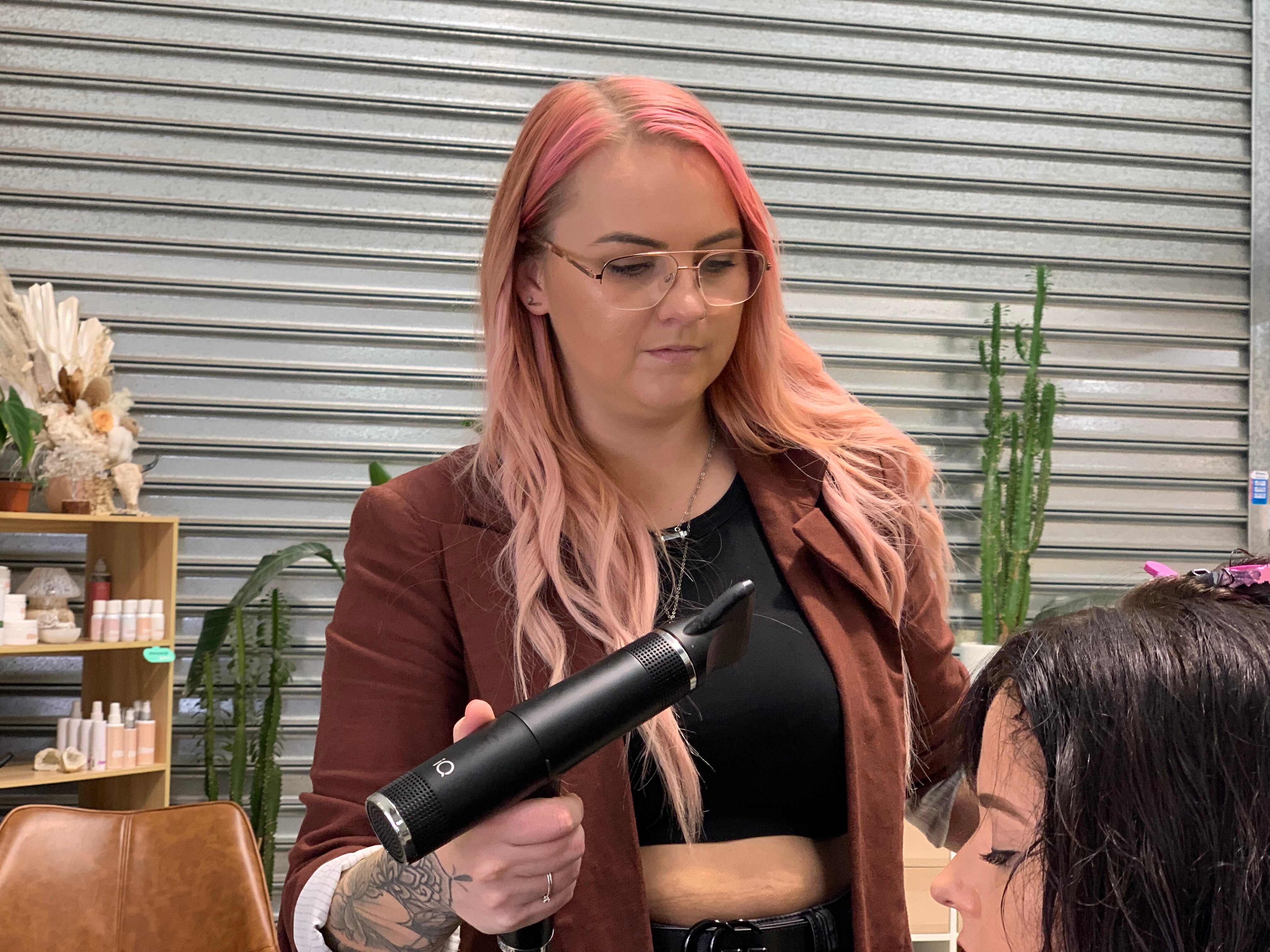 Woman with pink hair holding a hairdryer.
