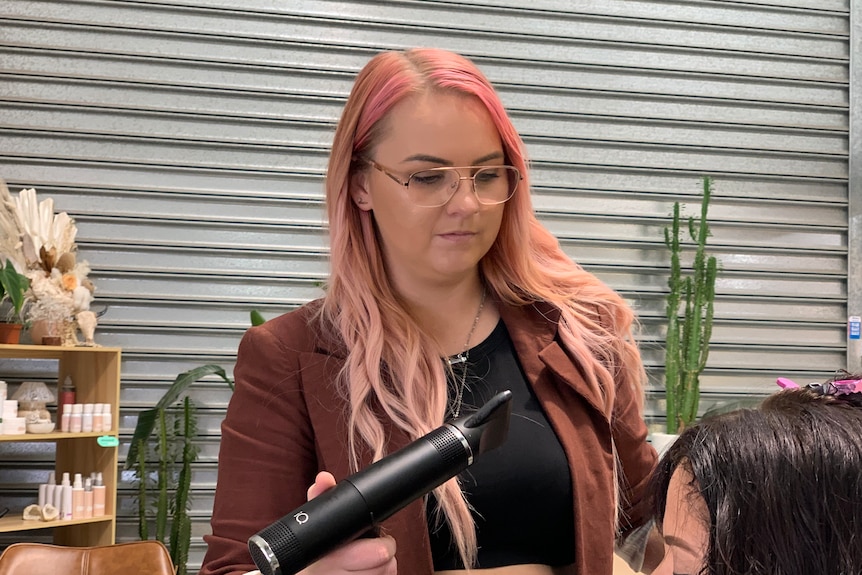 Woman with pink hair holding a hairdryer.