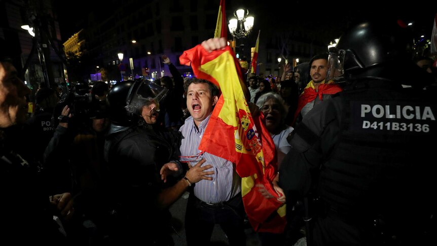 A pro-unity protestor is surrounded by police as he holds a Spanish flag and yells.