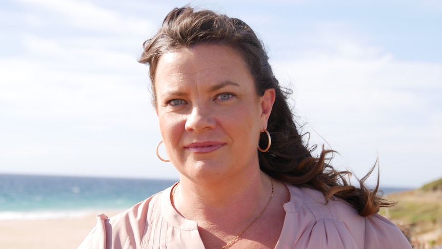 A woman with long brown hair stands at the beach.