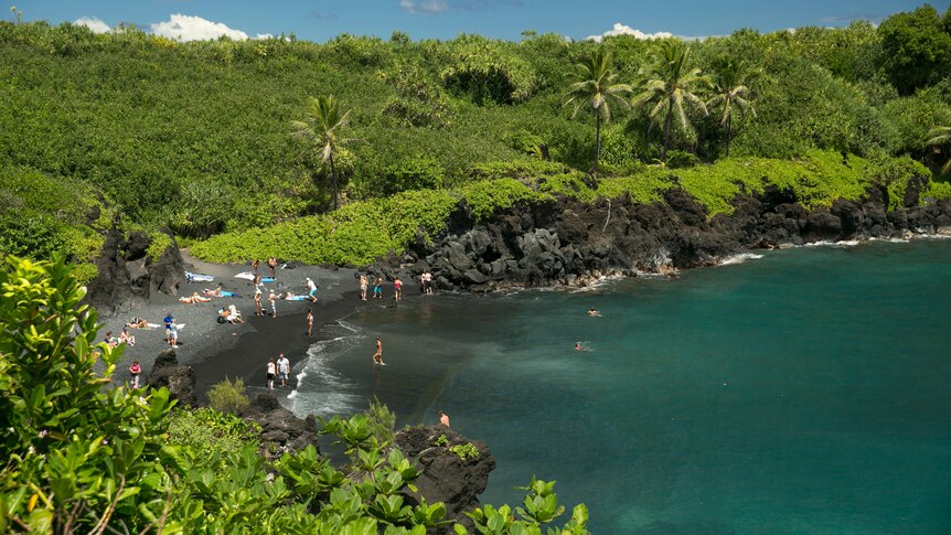 An aerial view of the coast at Waianapanapa State Park in Hana, Hawaii as people play on the beach