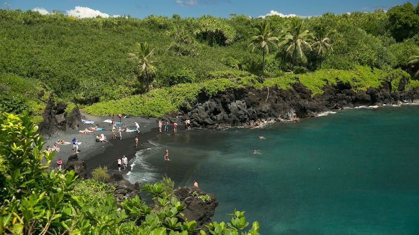 An aerial view of the coast at Waianapanapa State Park in Hana, Hawaii as people play on the beach