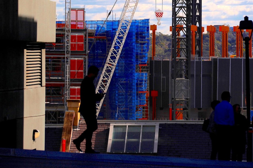 Pedestrians walk in front of a crane and on a construction site