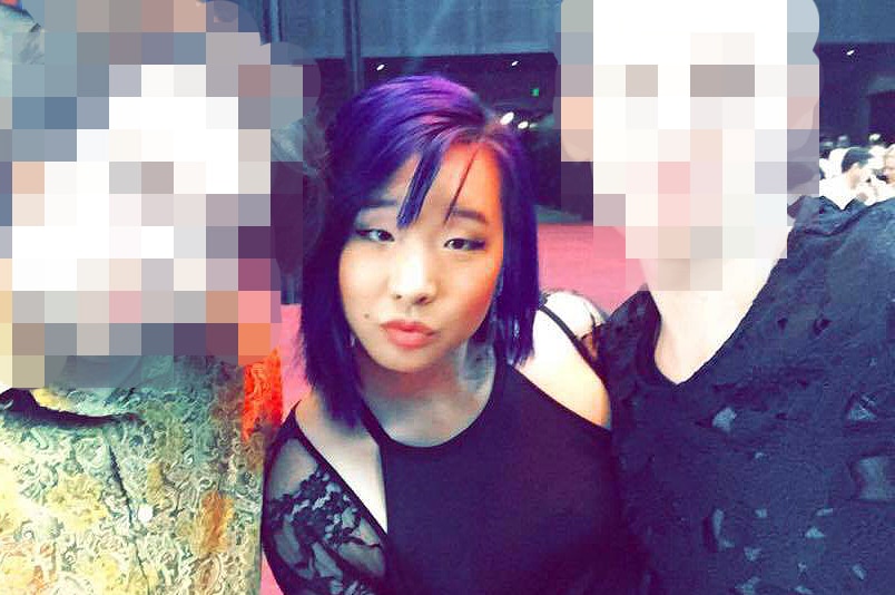 A young woman poses for a photo at a function in between two men whose faces are pixelated.