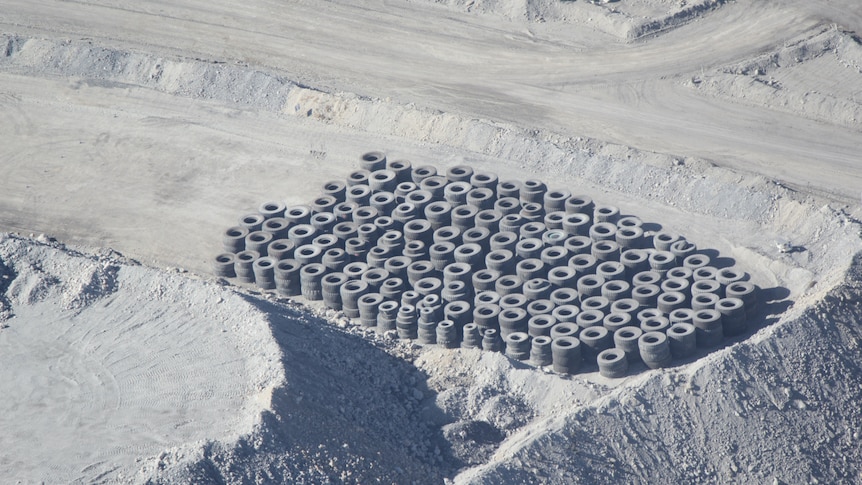 Several piles of tyres on a dirt strip next to an embankment, yet to be covered up.