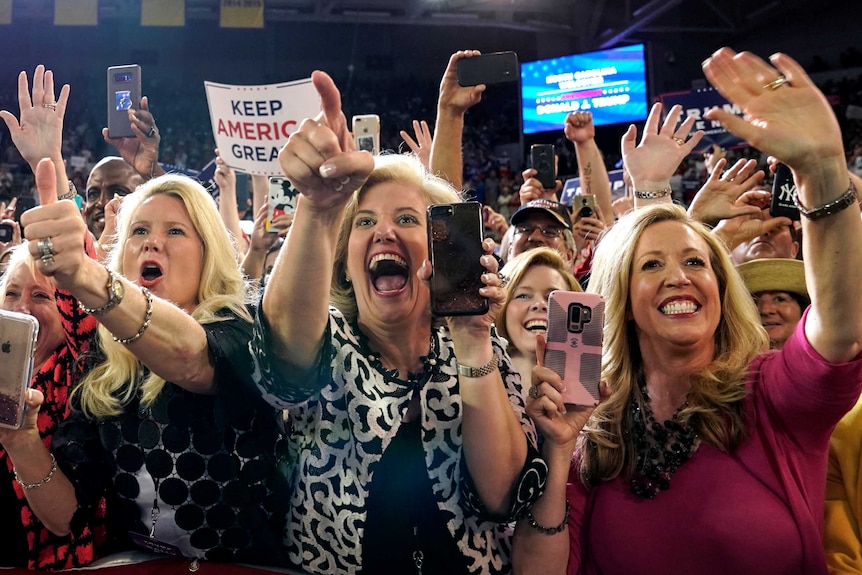 A group of people with their phones up cheering and holding "Keep America Great" signs