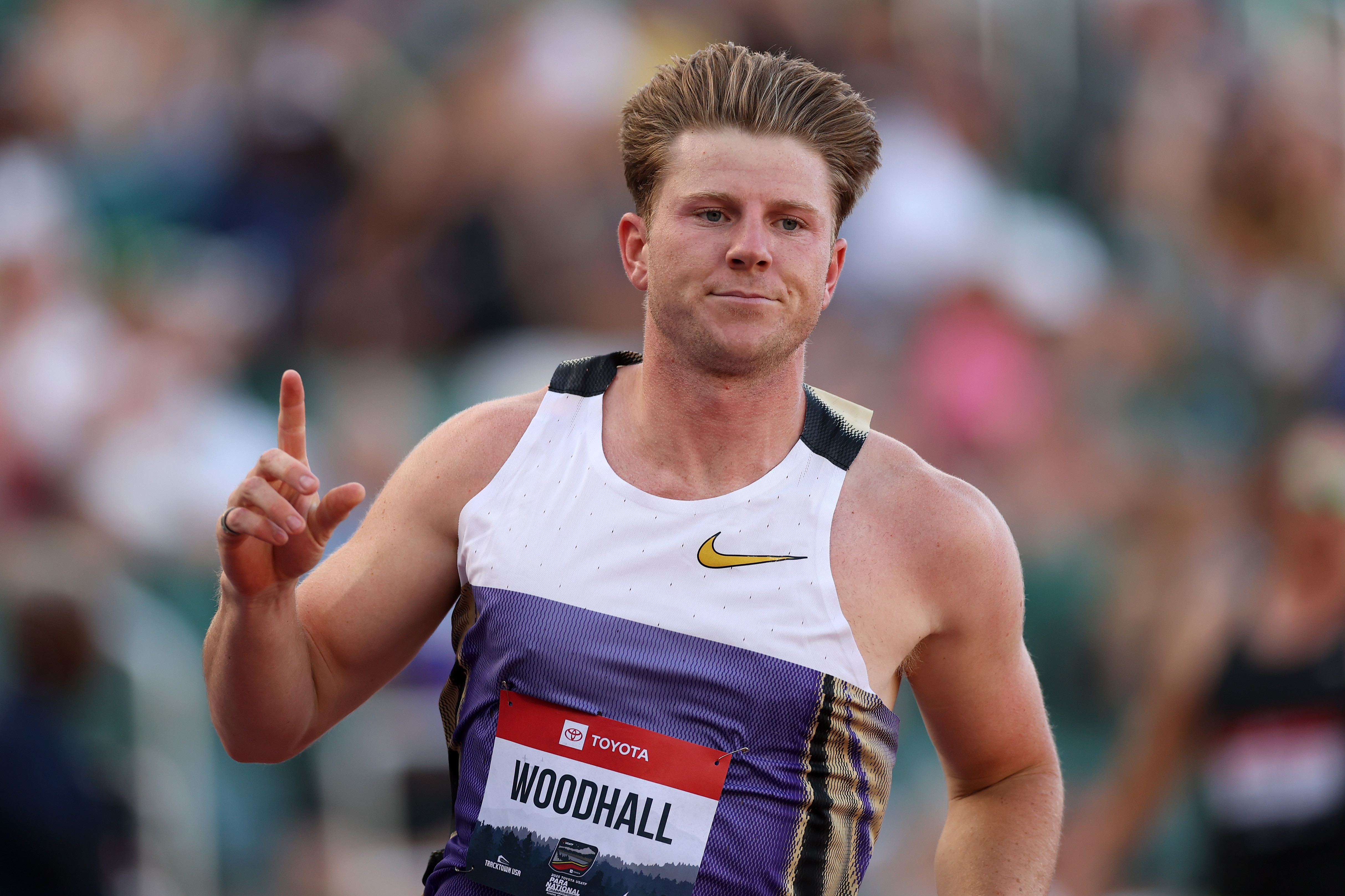 A man raises his hand in celebration as he finishes a track race in a stadium.