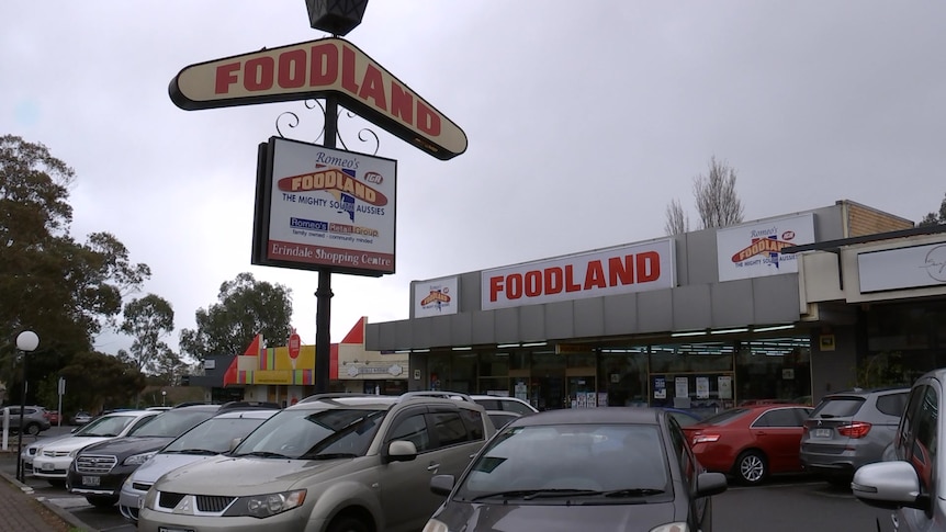 A supermarket sign on a post and a car park with the shop behind