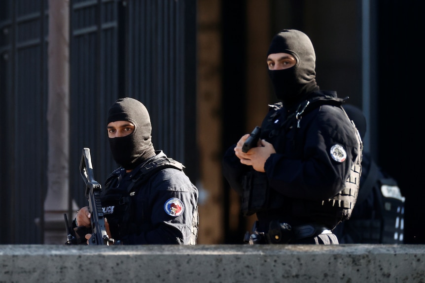 Two armed police officers wearing balaclavas stand guard outside a courthouse.