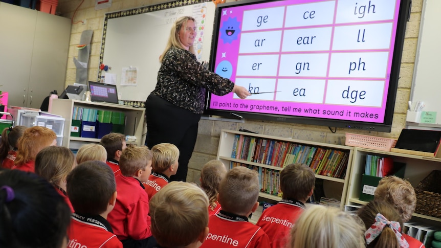 A woman pointing at a whiteboard in front of a young glass