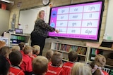 A woman pointing at a whiteboard in front of a young glass