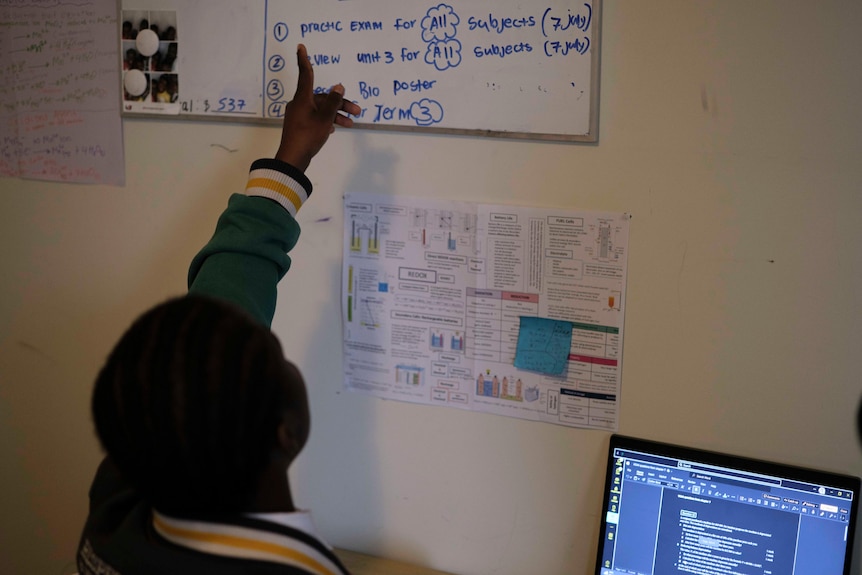 A girl points at her whiteboard with a schoolwork to-do list