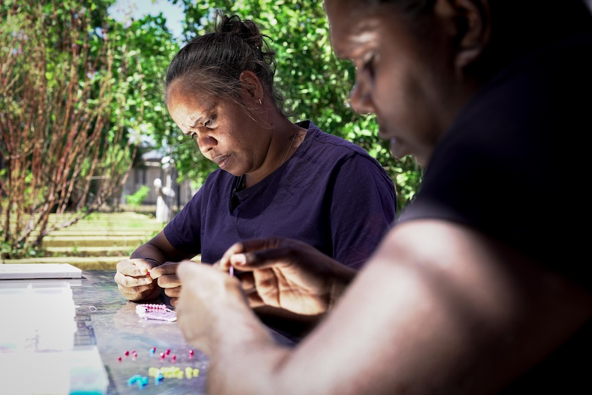 two aboriginal women making bracelets at a table