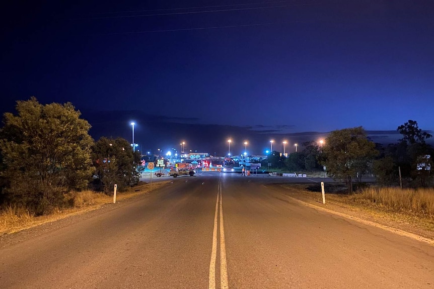 A road leading the an entrance of the mine site, which has lots of street lights and signs.