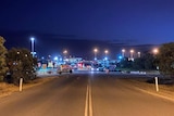 A road leading the an entrance of the mine site, which has lots of street lights and signs.