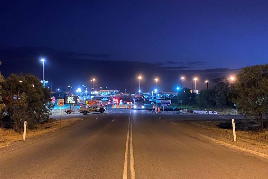 A road leading the an entrance of the mine site, which has lots of street lights and signs.