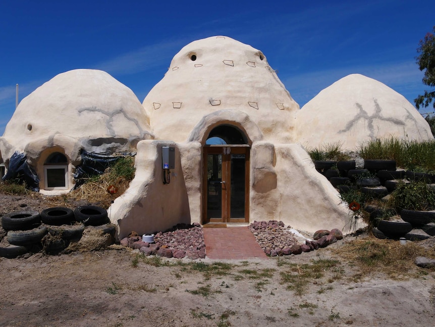 A cream coloured dome shaped home in front of a blue sky.