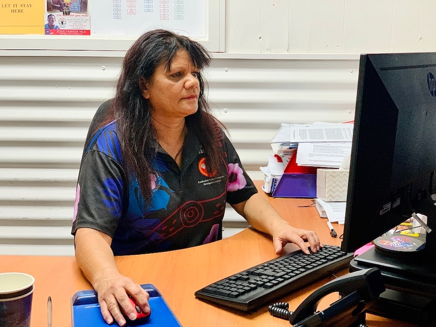 Image of a woman with long brown hair, sitting at a desk whilst operating a computer.