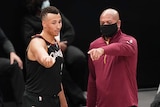 A mask-wearing NBA coach points as he speaks to one of his players at courtside during a game.