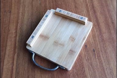 A chopping board with a stainless steel handle and protruded wooden edging on two converging sides