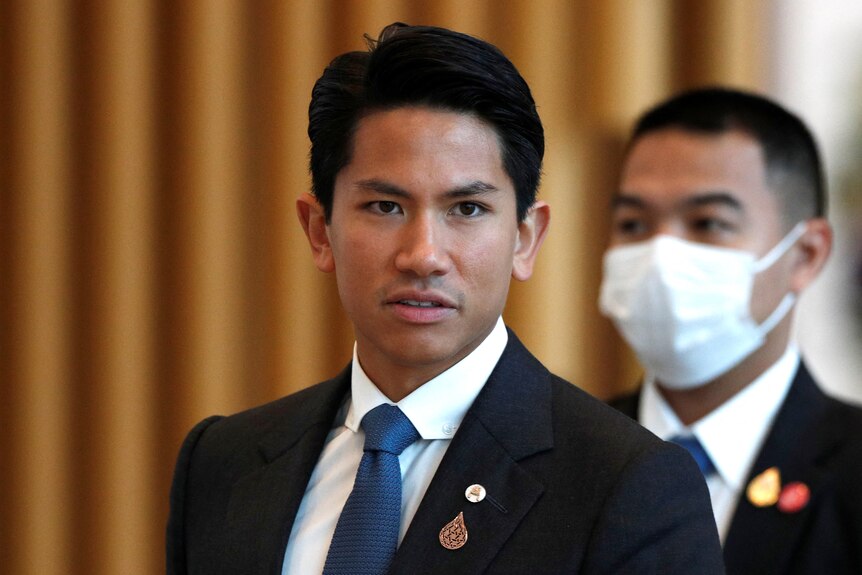 Brunei's Prince Mateen wears a black suit and blue tie and gazes at the camera. 